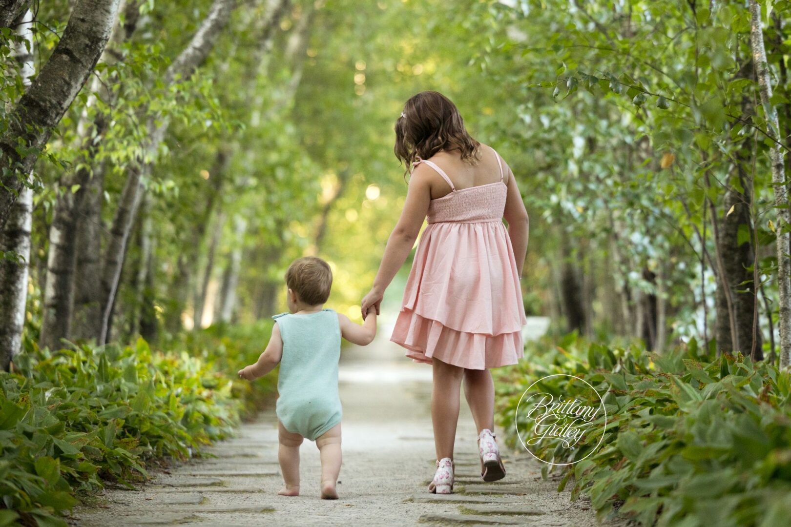 Big sister walking her baby brother hand in hand down the birch tree path at Stan Hywet
