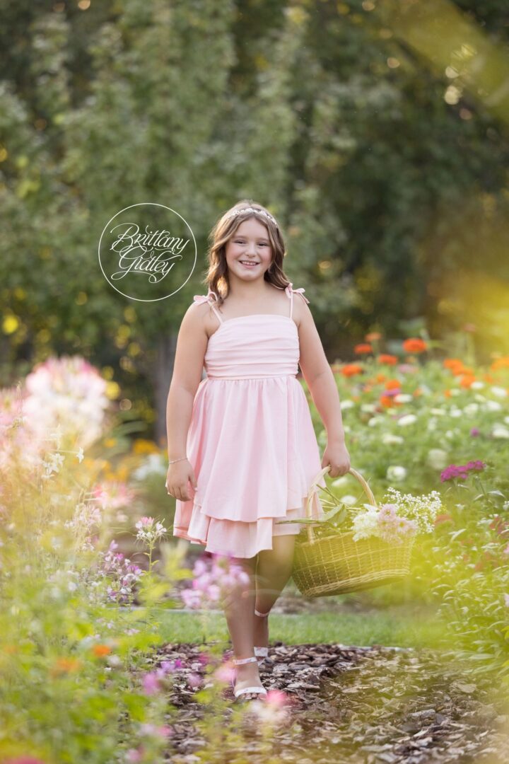 Girl in a pink dress carrying a flower basket through a colorful garden in Akron, Ohio
