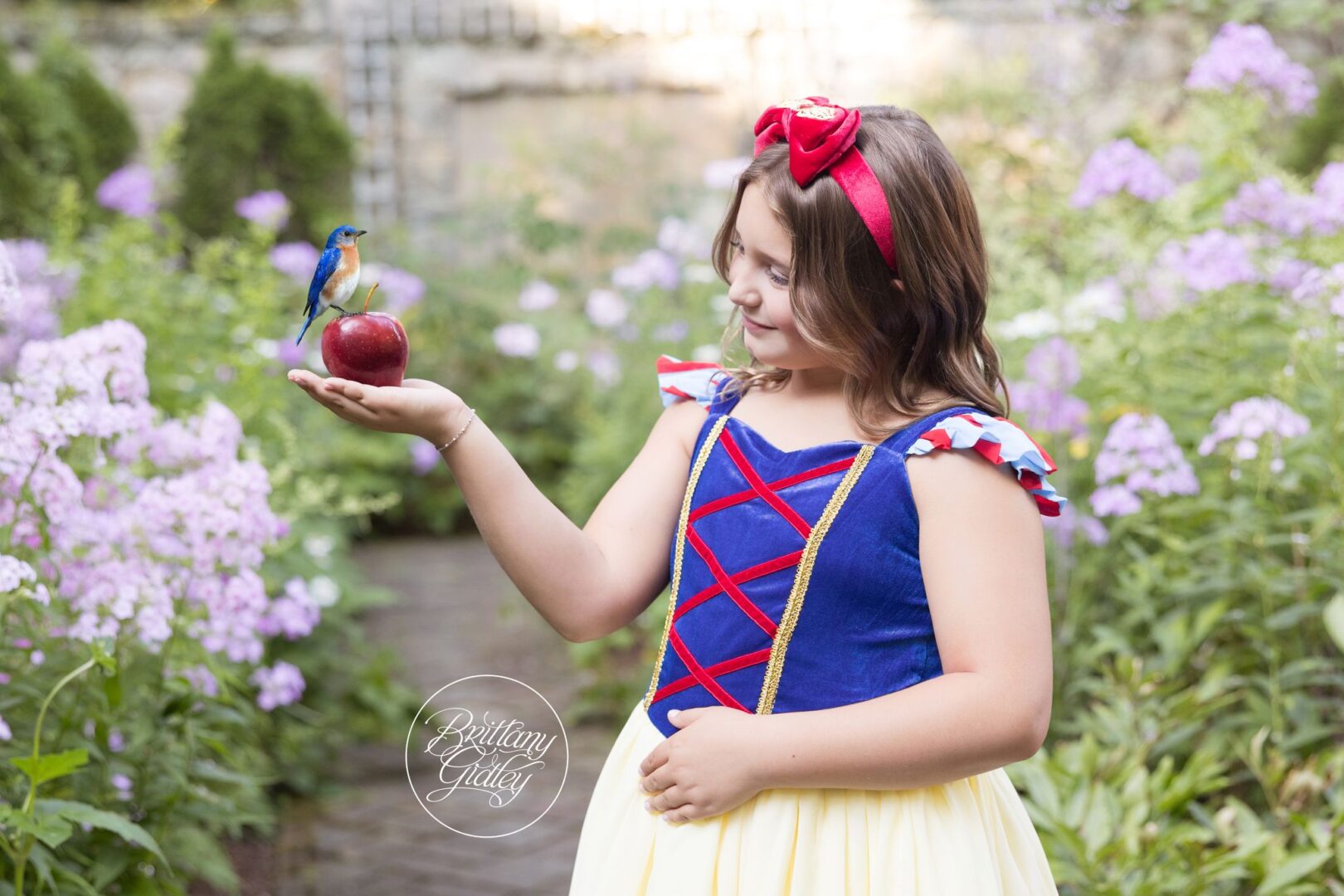 Girl dressed as Snow White holding a red apple with a bluebird in a garden at Stan Hywet
