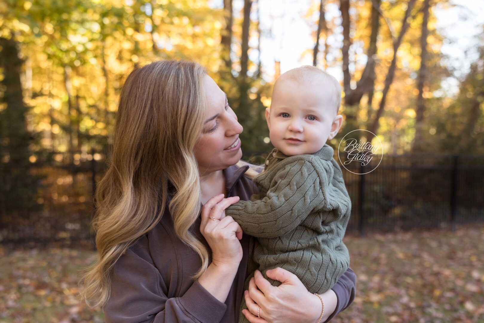 Mom holding baby Nolan in a green knit sweater among the fall leaves