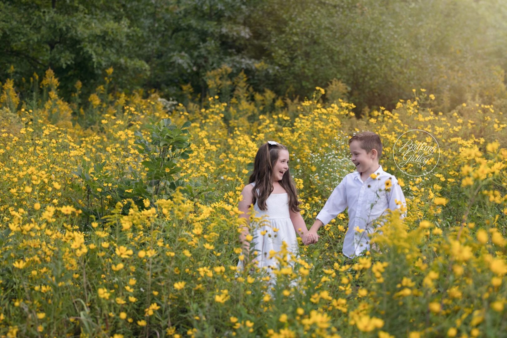 Siblings holding hands and laughing among yellow wildflowers at Bay Field in Bay Village