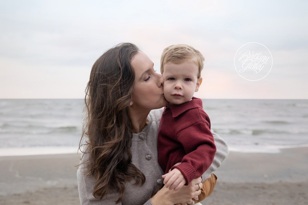 Mom kissing her toddler son in a red sweater on a Lake Erie beach