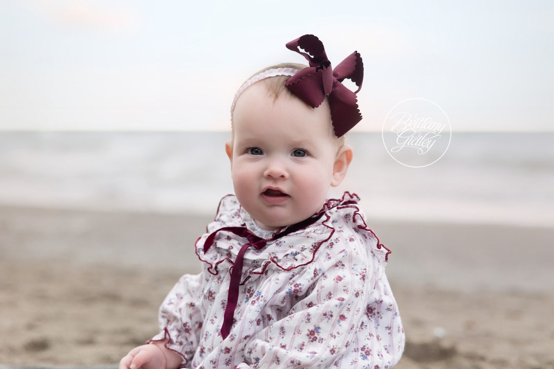 Baby girl sitting on the sand at Huntington Beach during a family photo session