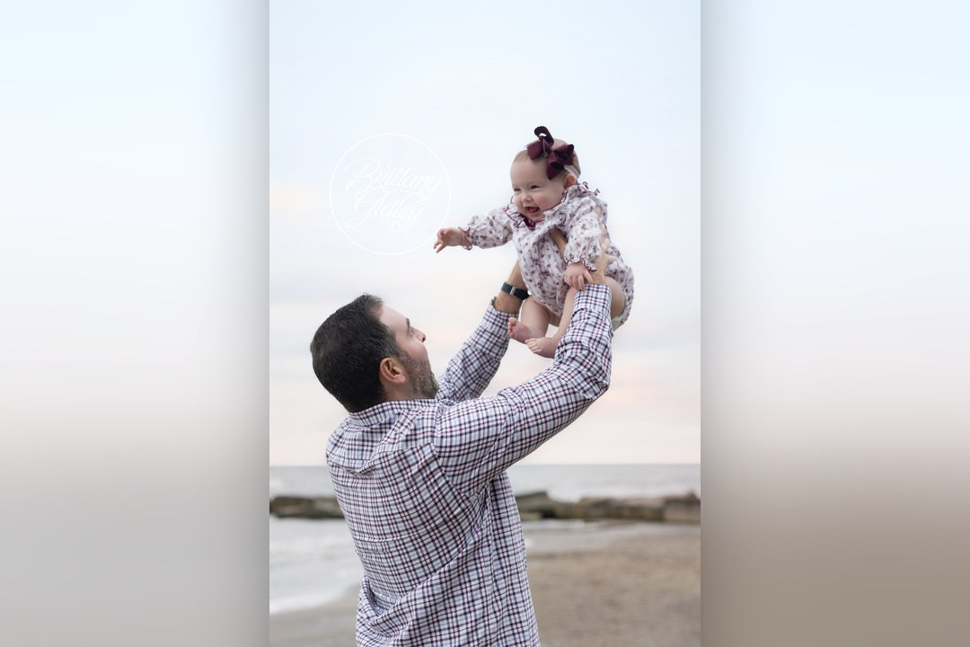Dad lifting his baby daughter toward the sky on the Lake Erie shoreline
