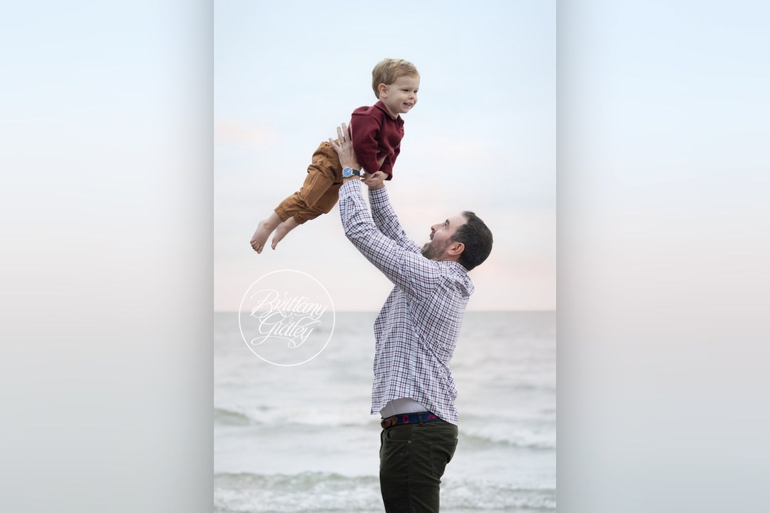 Dad tossing his toddler son in the air on the beach in Bay Village