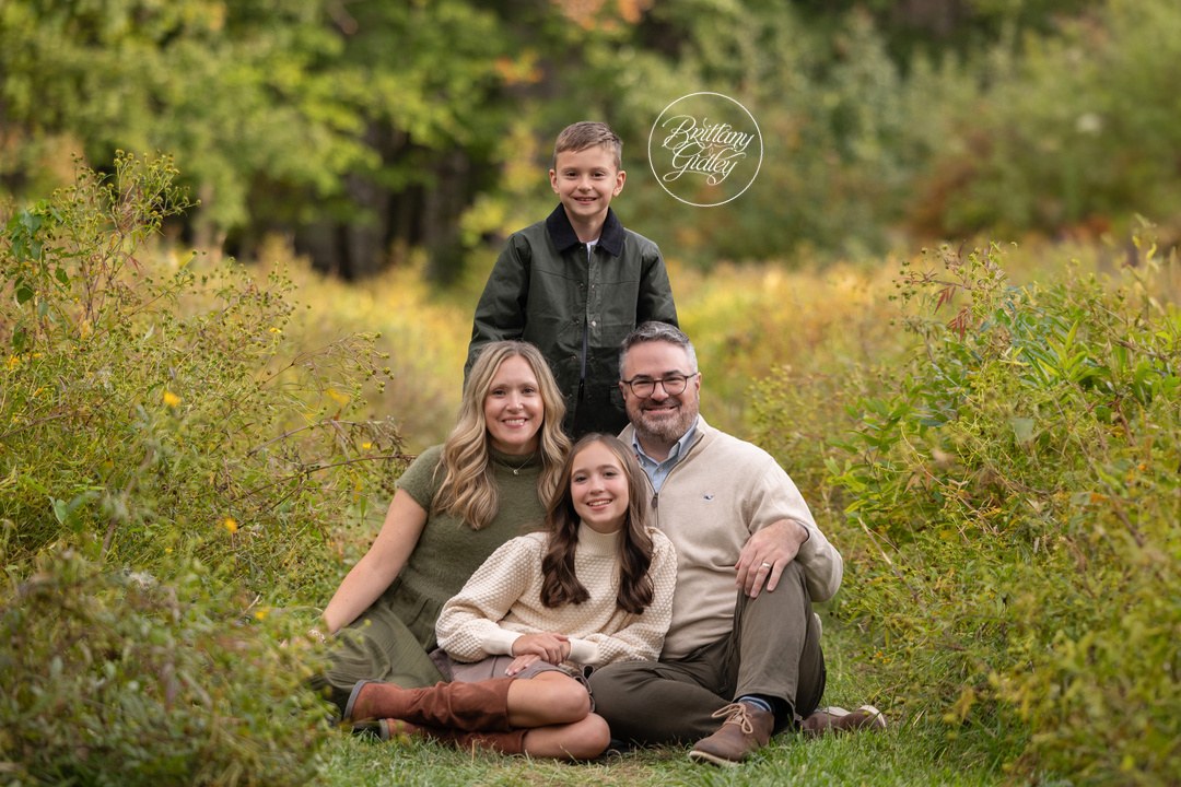 Family sitting together in the grass with fall trees behind them in Bay Village