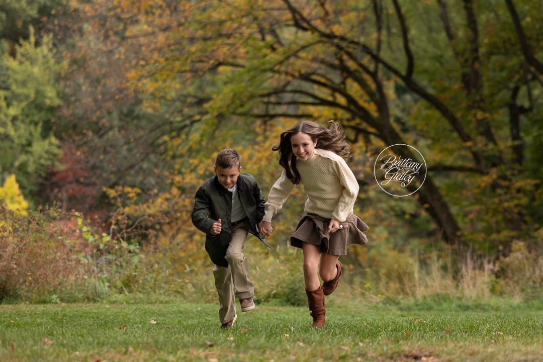 Brother and sister running hand in hand across the field, birthday photo shoot