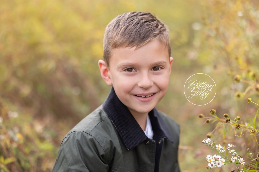 Smiling boy in a green jacket with autumn wildflowers behind him