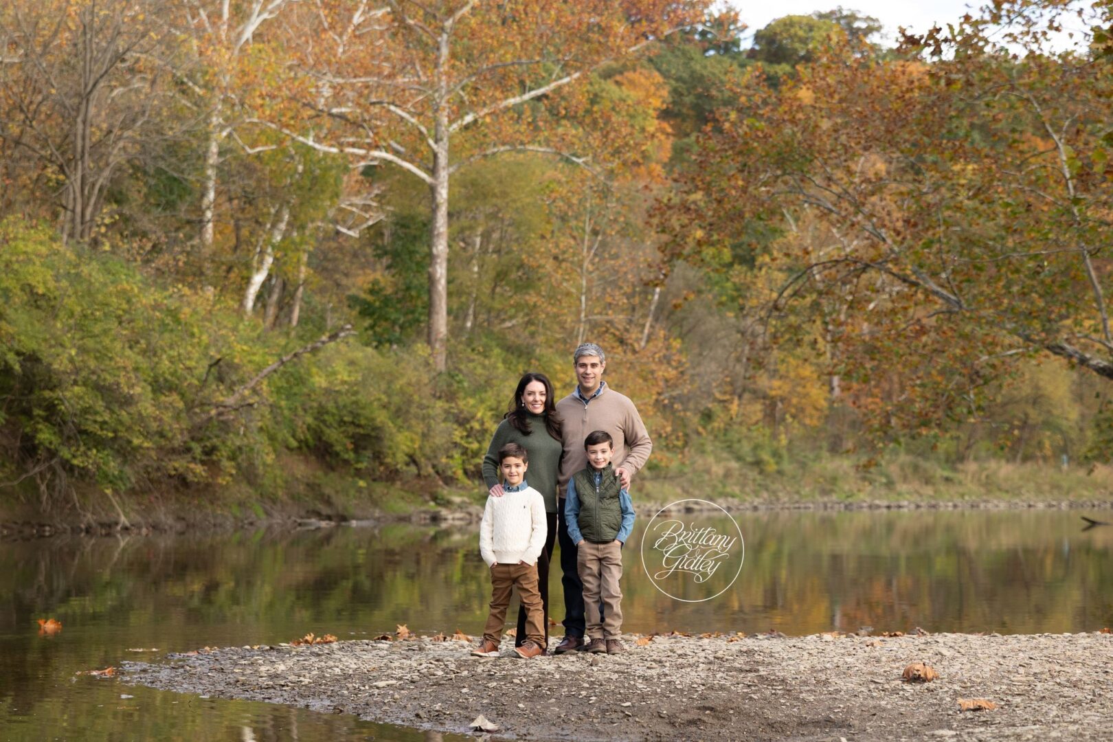 Arnold family of four standing by the Cuyahoga River in fall at Brecksville Reservation