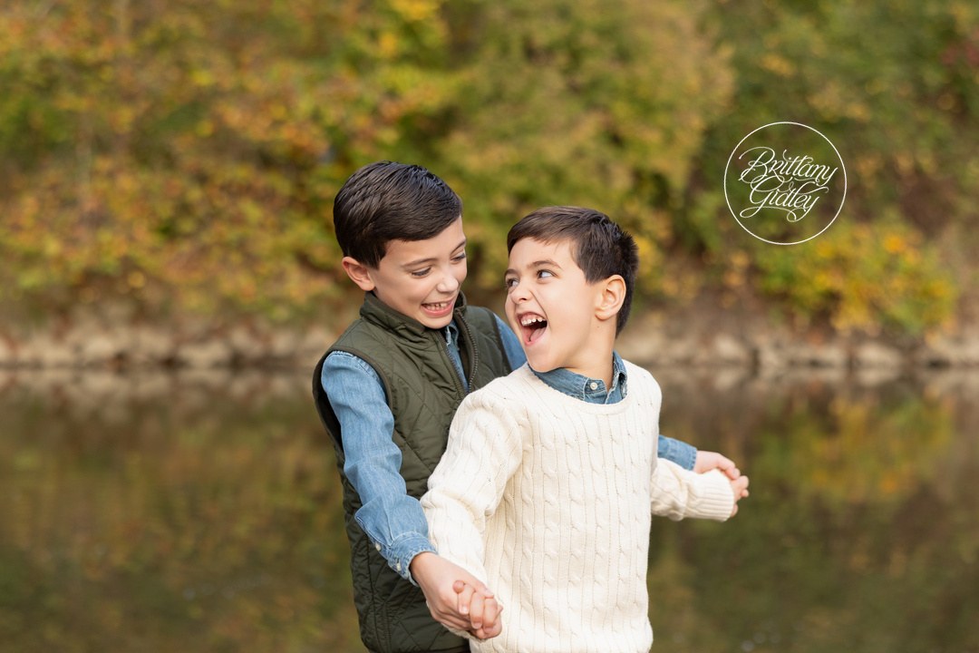 Brothers laughing together by the water with fall colors behind them