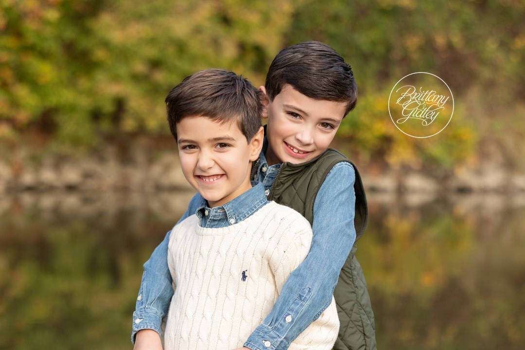 Big brother hugging little brother from behind by the river in autumn