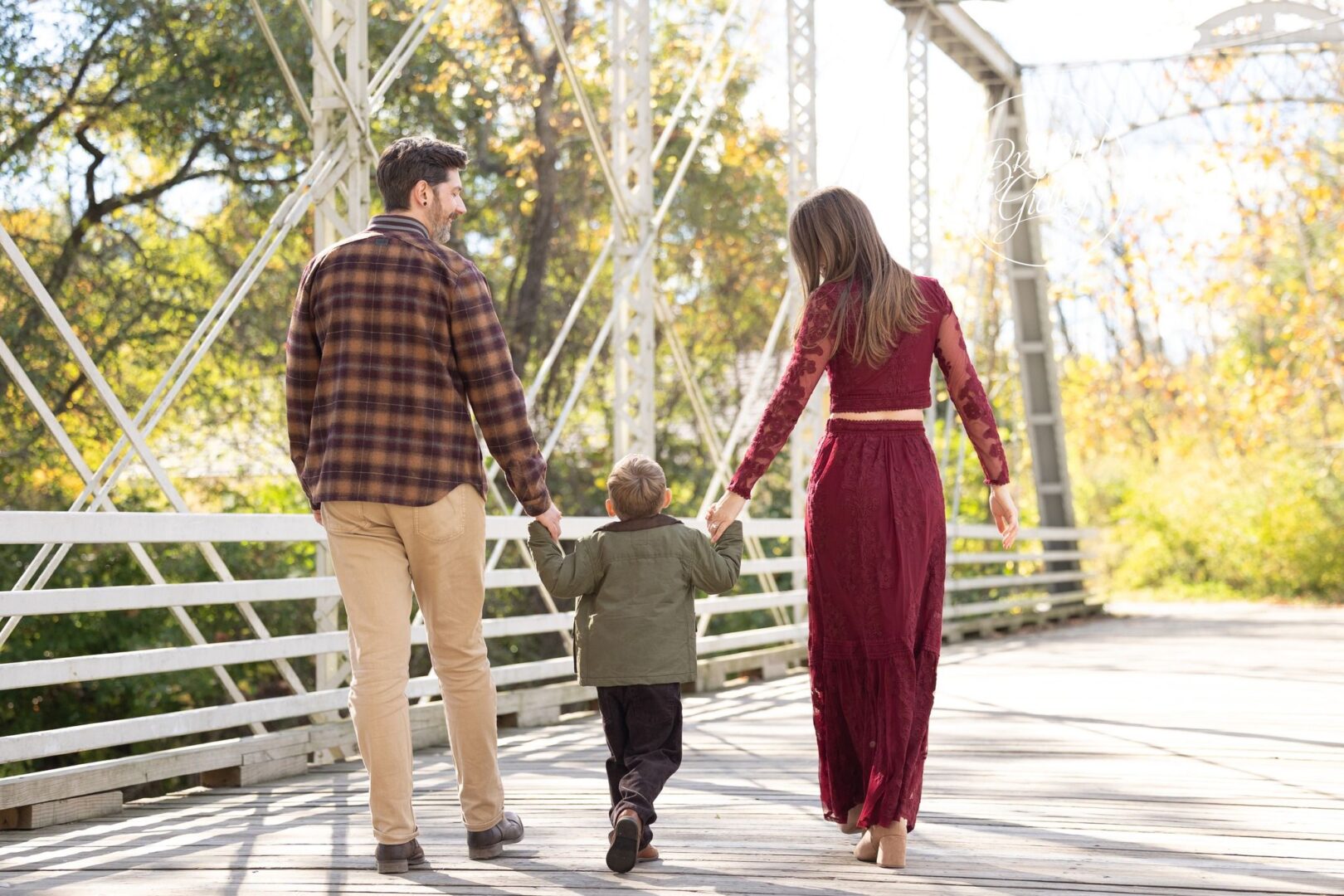 Mom and Dad walking hand in hand with their son across the white bridge at Brecksville Reservation
