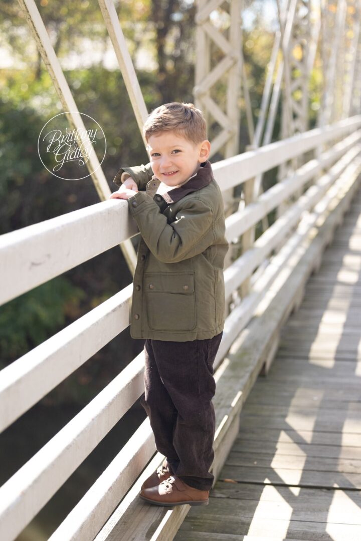 Little boy in a green jacket leaning on the white bridge railing at Brecksville Reservation