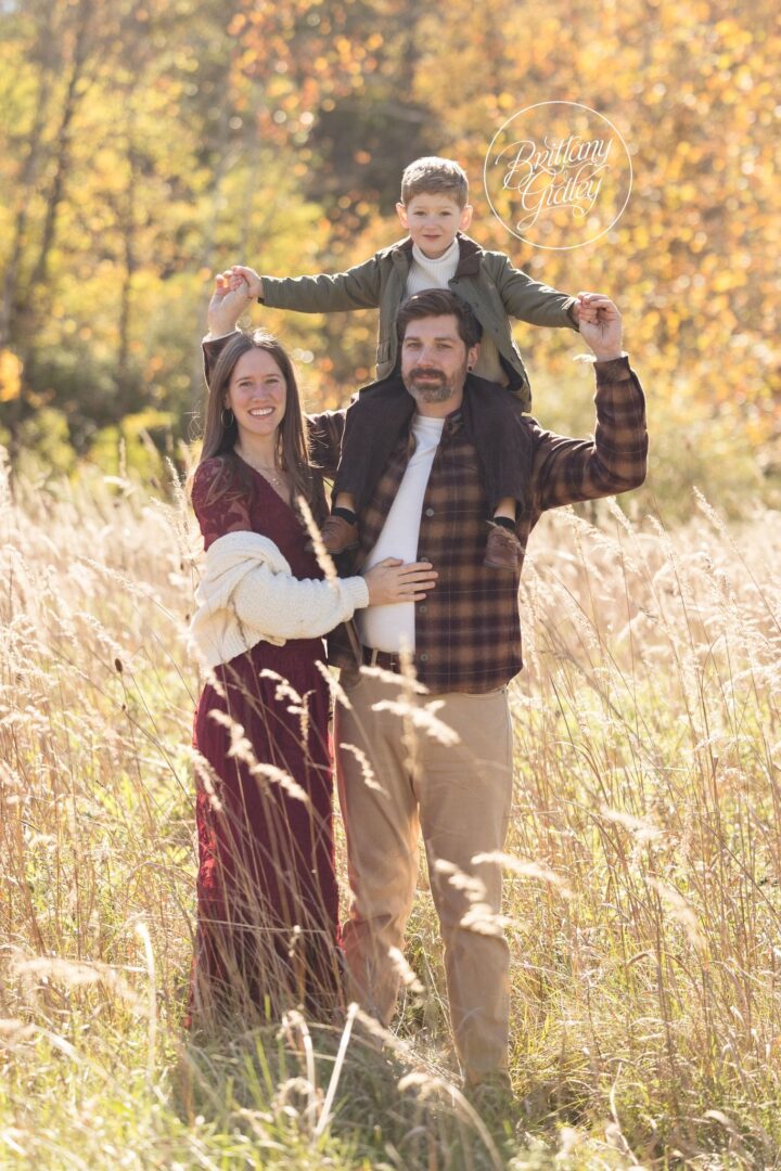 Little boy riding on Dad's shoulders with Mom beside them in a golden fall field at Brecksville Reservation