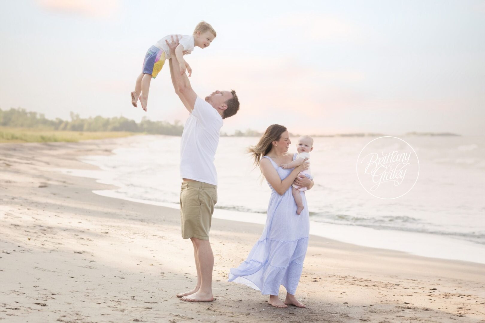 Dad lifting Miles into the air while Mom holds Nolan on the beach