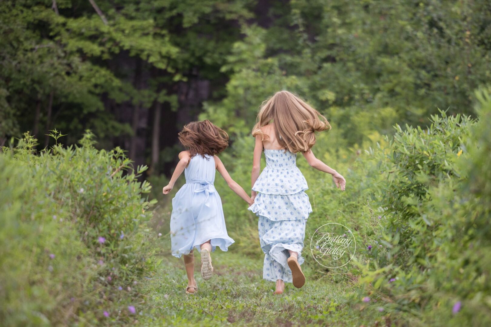 Two sisters skipping down a grassy path in matching blue dresses at Bay Field