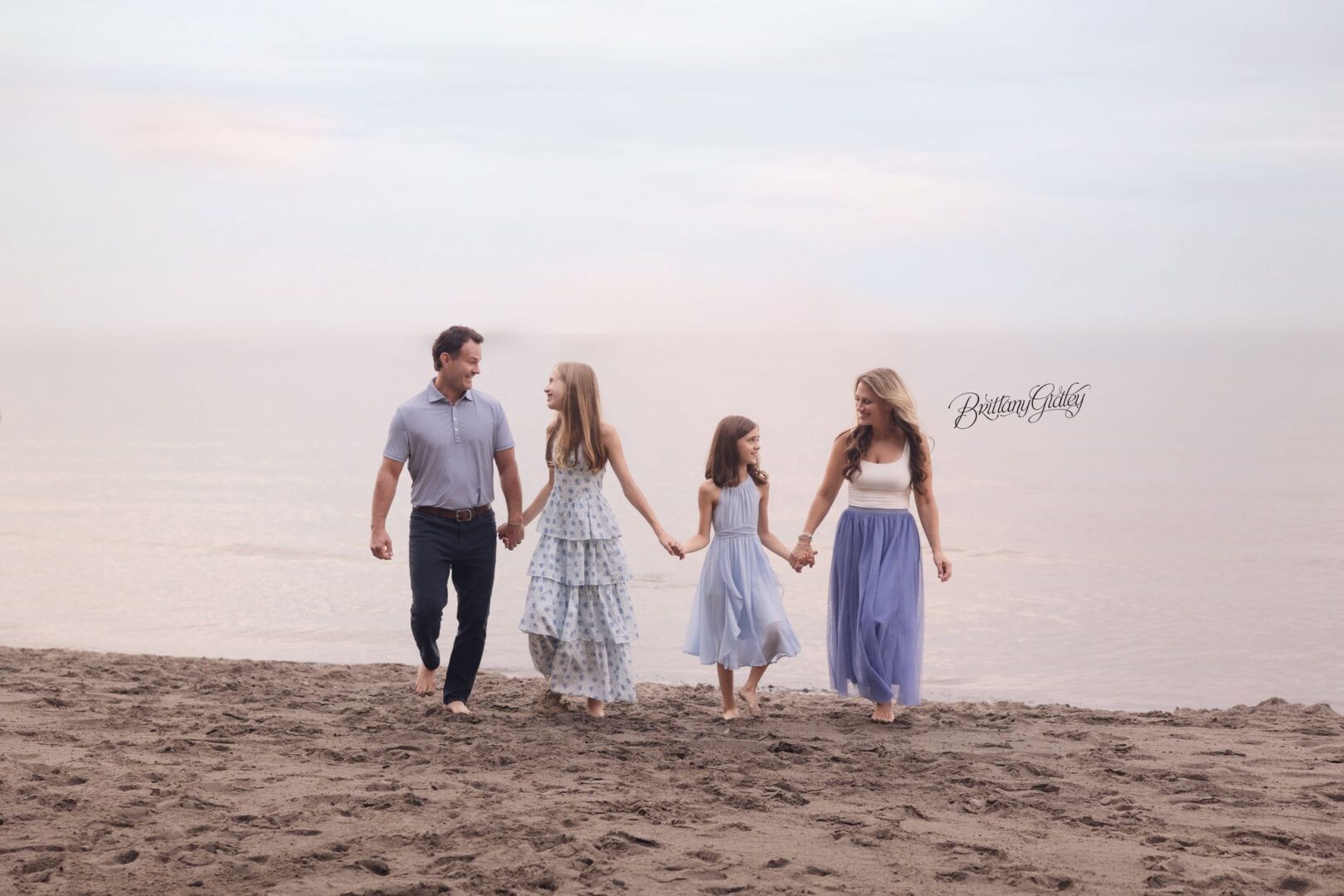 Family of four walking hand in hand along Huntington Beach at sunset on Lake Erie