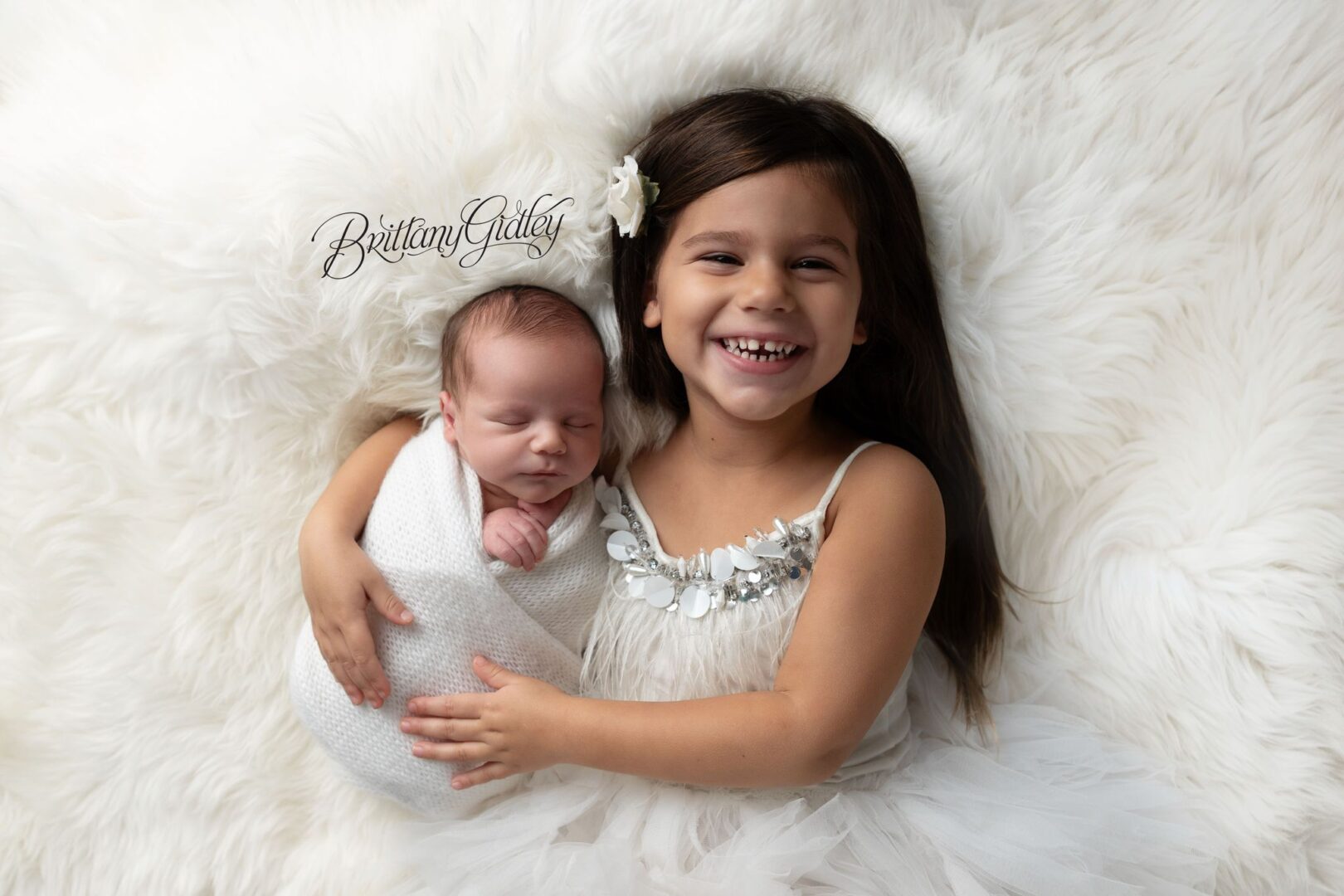 Big sister Penny hugging her newborn brother Theodore on a white fur blanket, Erie PA newborn photographer