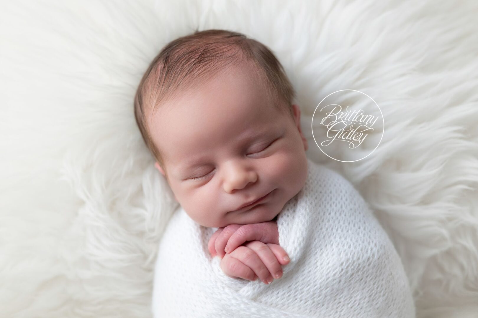 Close-up of a sleeping newborn boy with his hands tucked under his chin on white fur