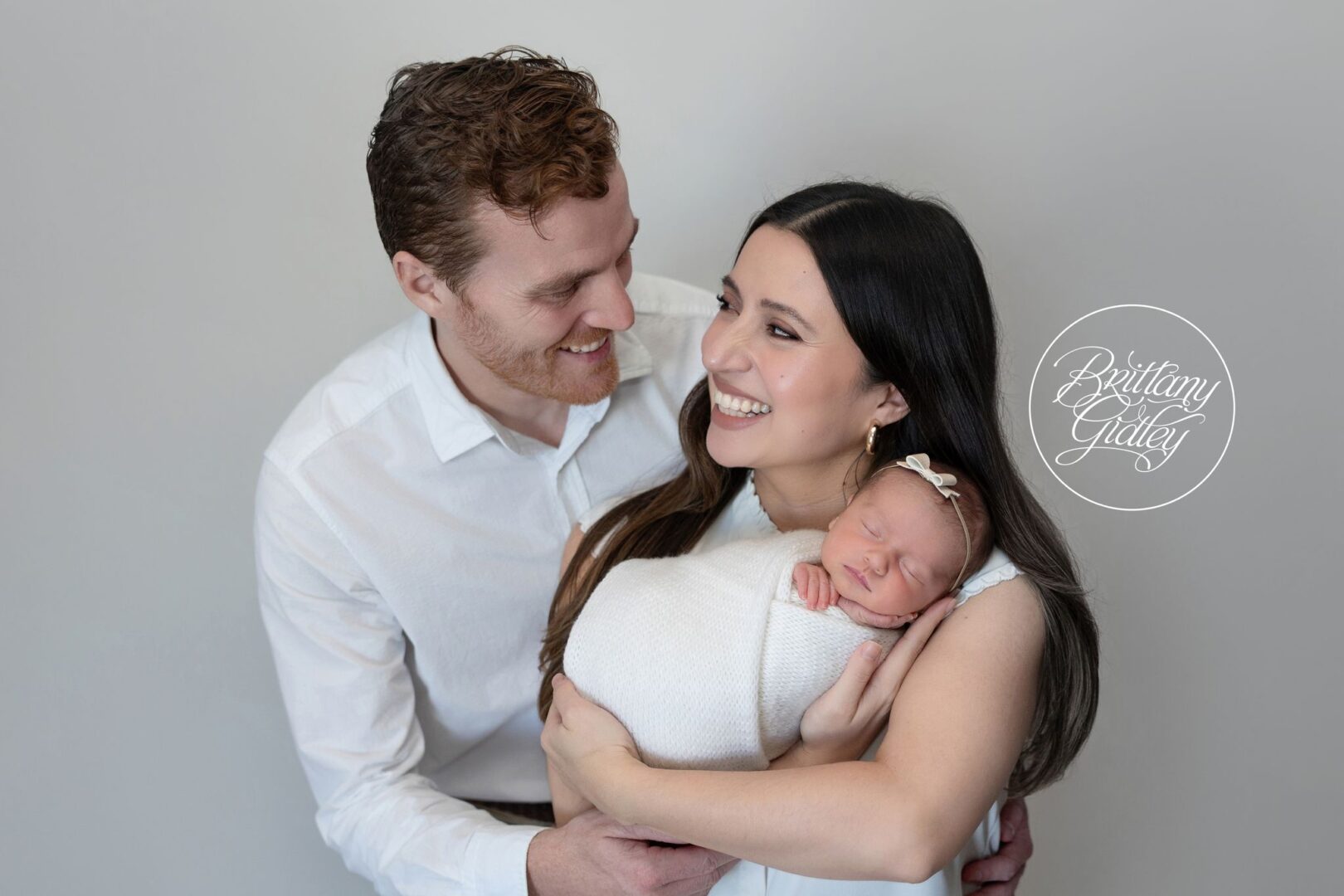 Mom and Dad smiling at each other while holding newborn Isabel