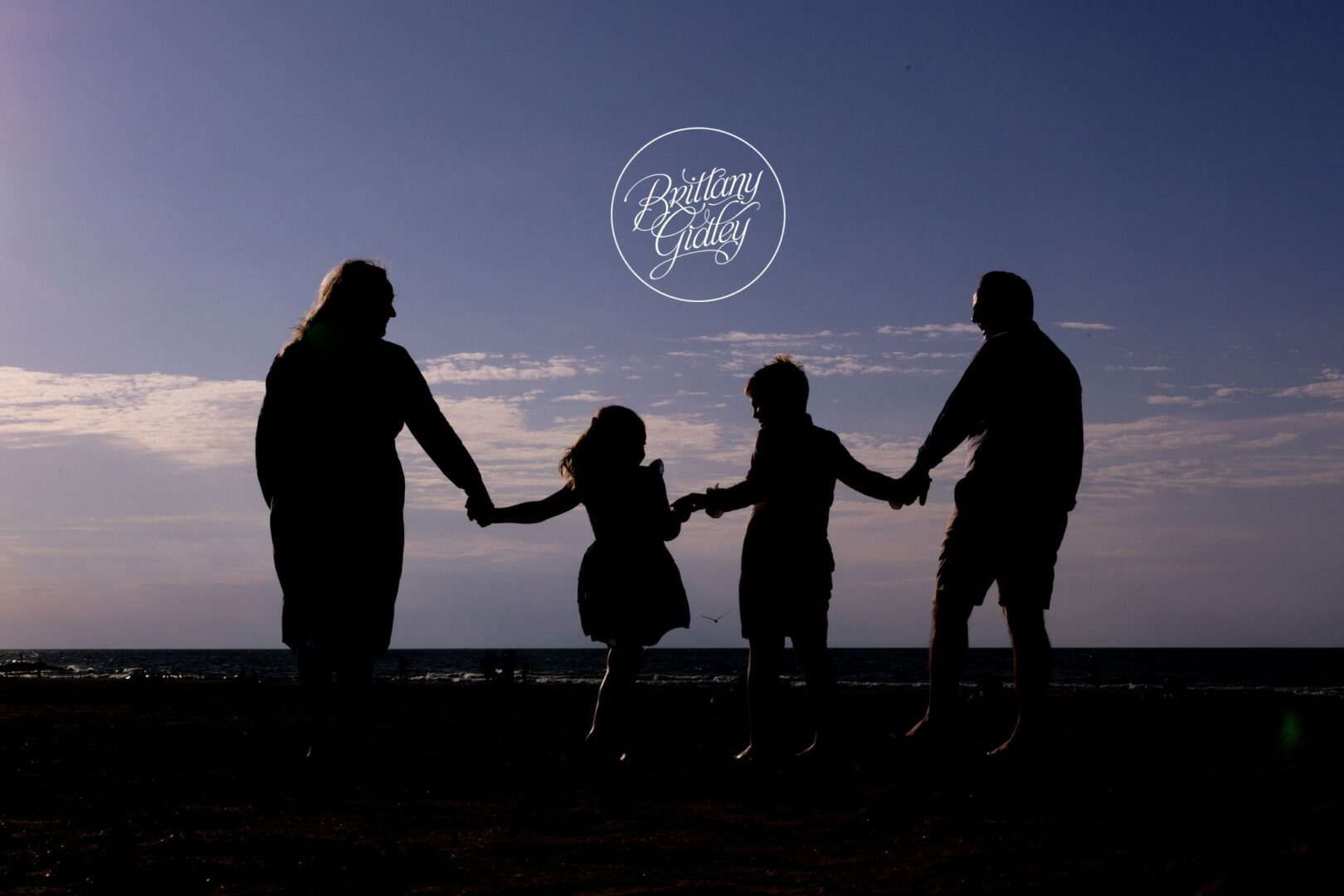 Family silhouette holding hands on Edgewater Beach at dusk