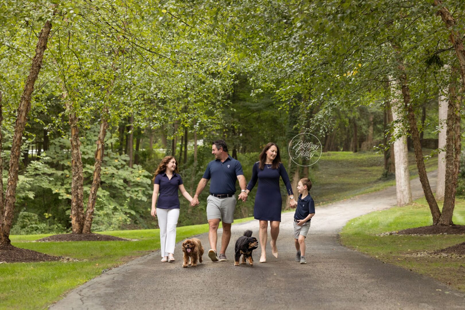 Reed family walking down their tree-lined driveway with their two Cavalier King Charles spaniels in Gates Mills, Ohio
