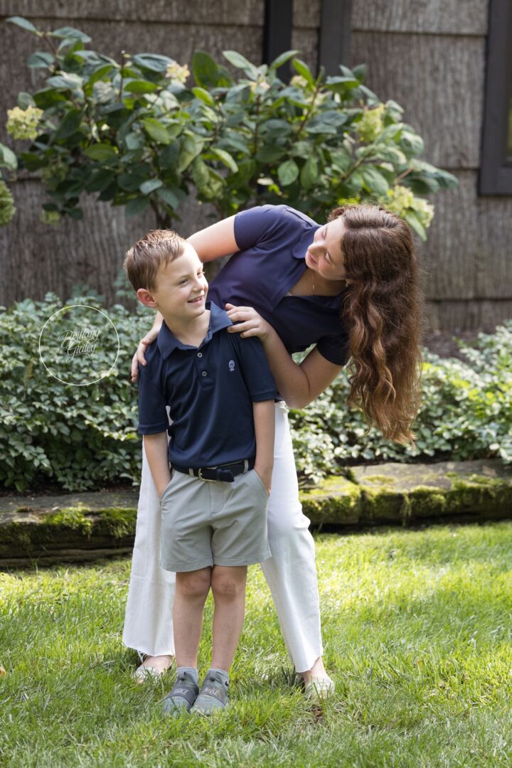 Sister playfully leaning over her little brother in front of the garden at their Gates Mills home