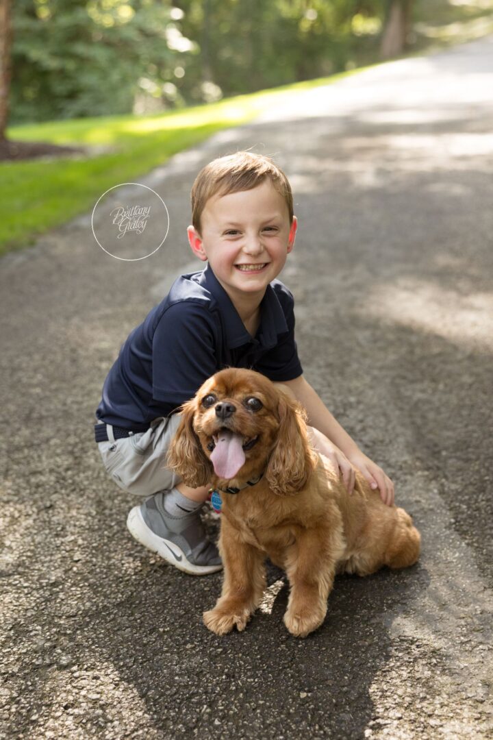 Smiling boy kneeling on the driveway with his ruby Cavalier King Charles spaniel