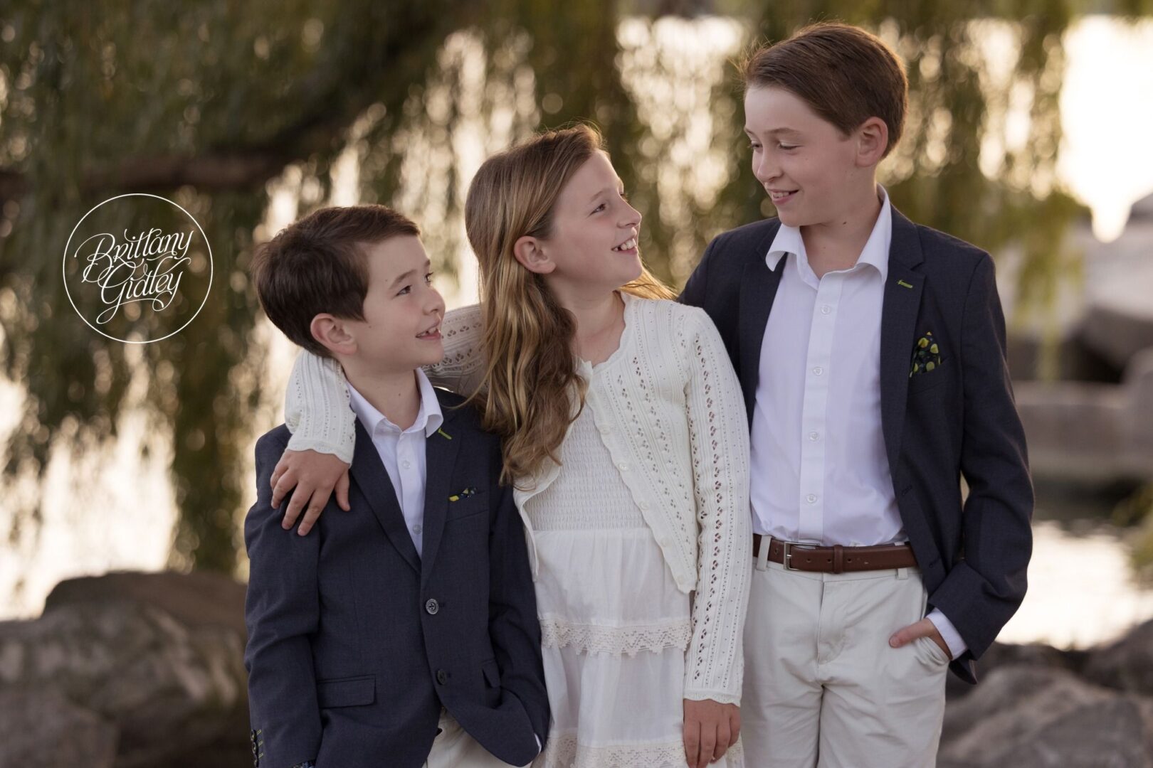 Three siblings laughing together under a willow tree on Lake Erie