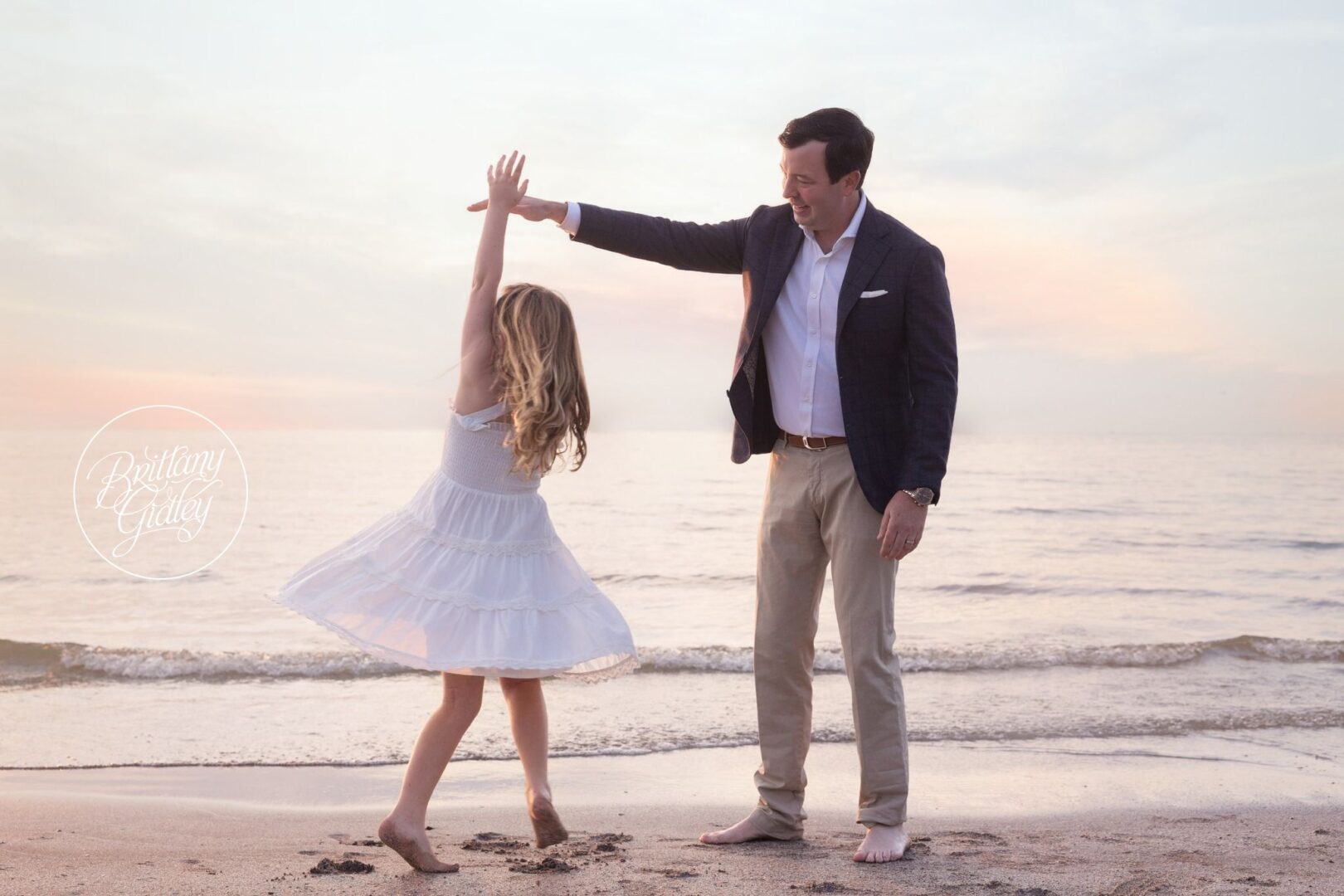 Dad twirling his daughter in the sand at sunset on Lake Erie