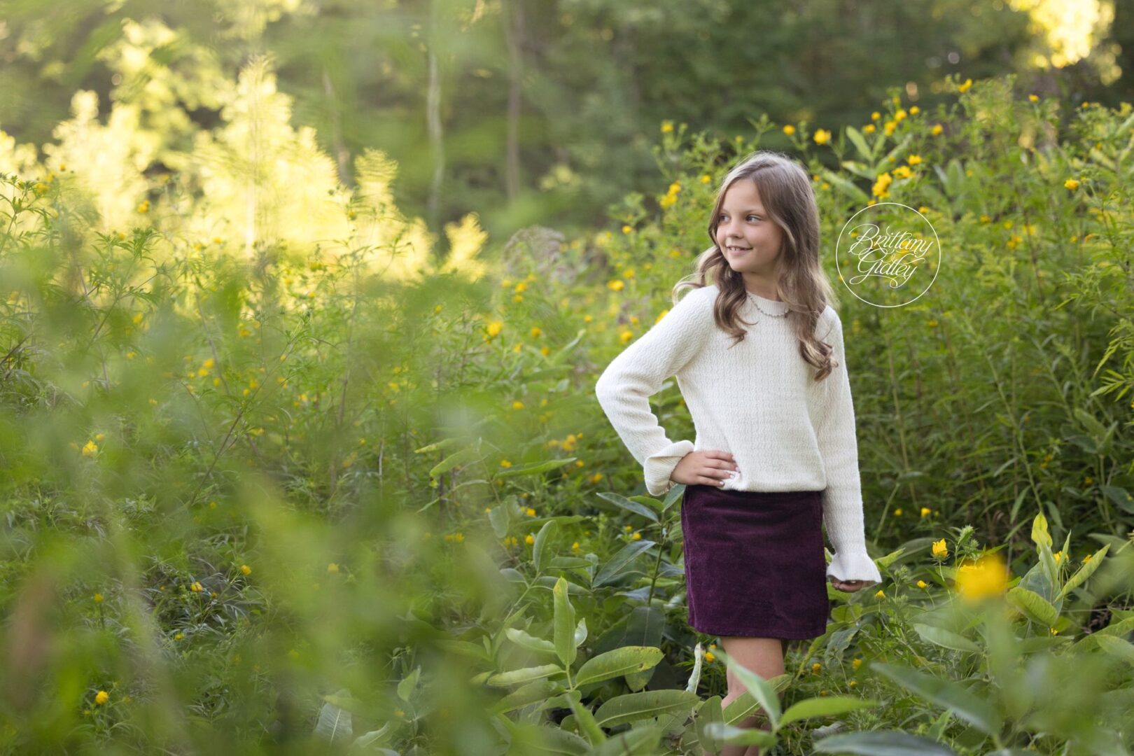 Girl in a cream sweater and burgundy skirt posing in yellow wildflowers at Bay Field