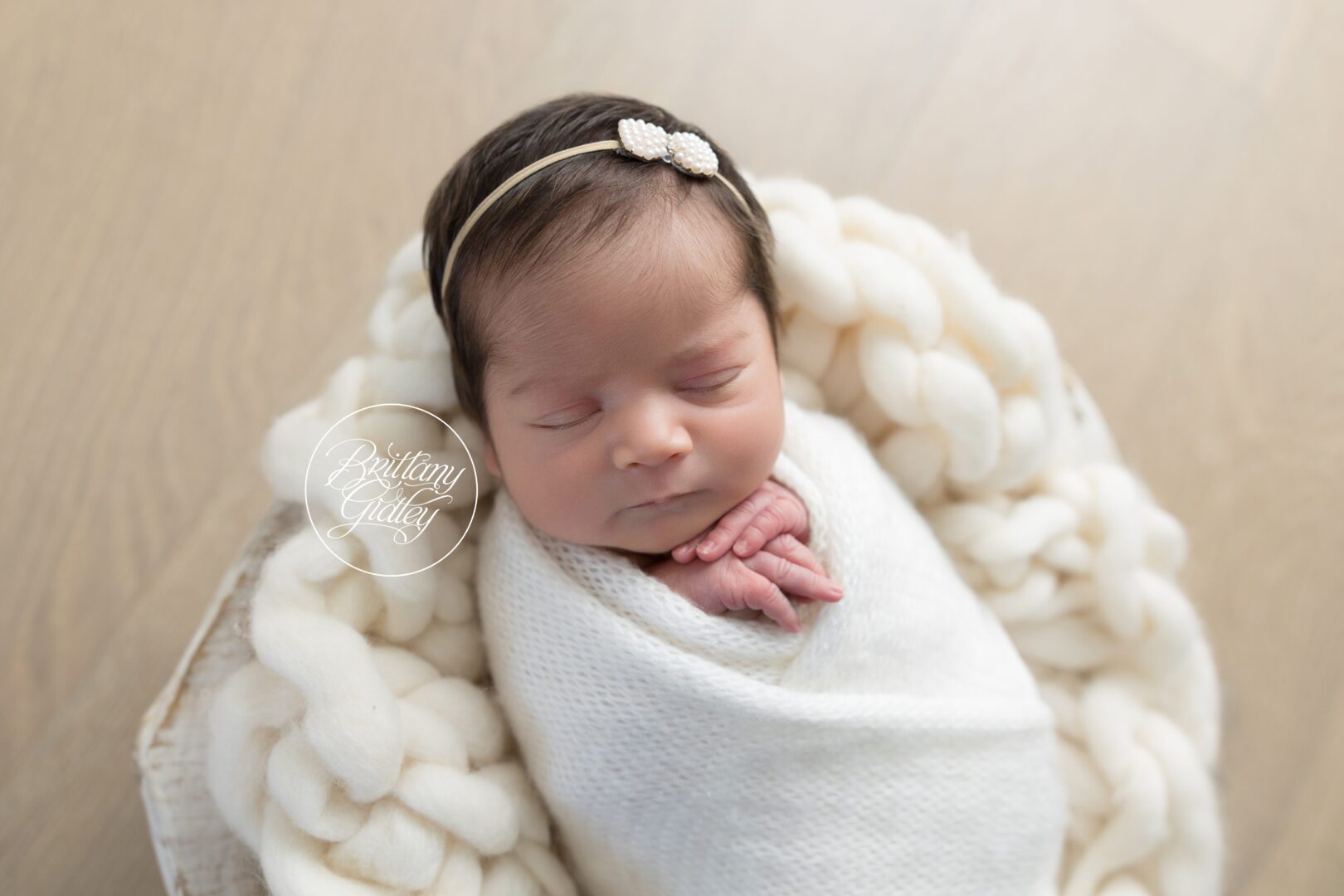 Newborn Ava sleeping swaddled in cream inside a chunky knit basket