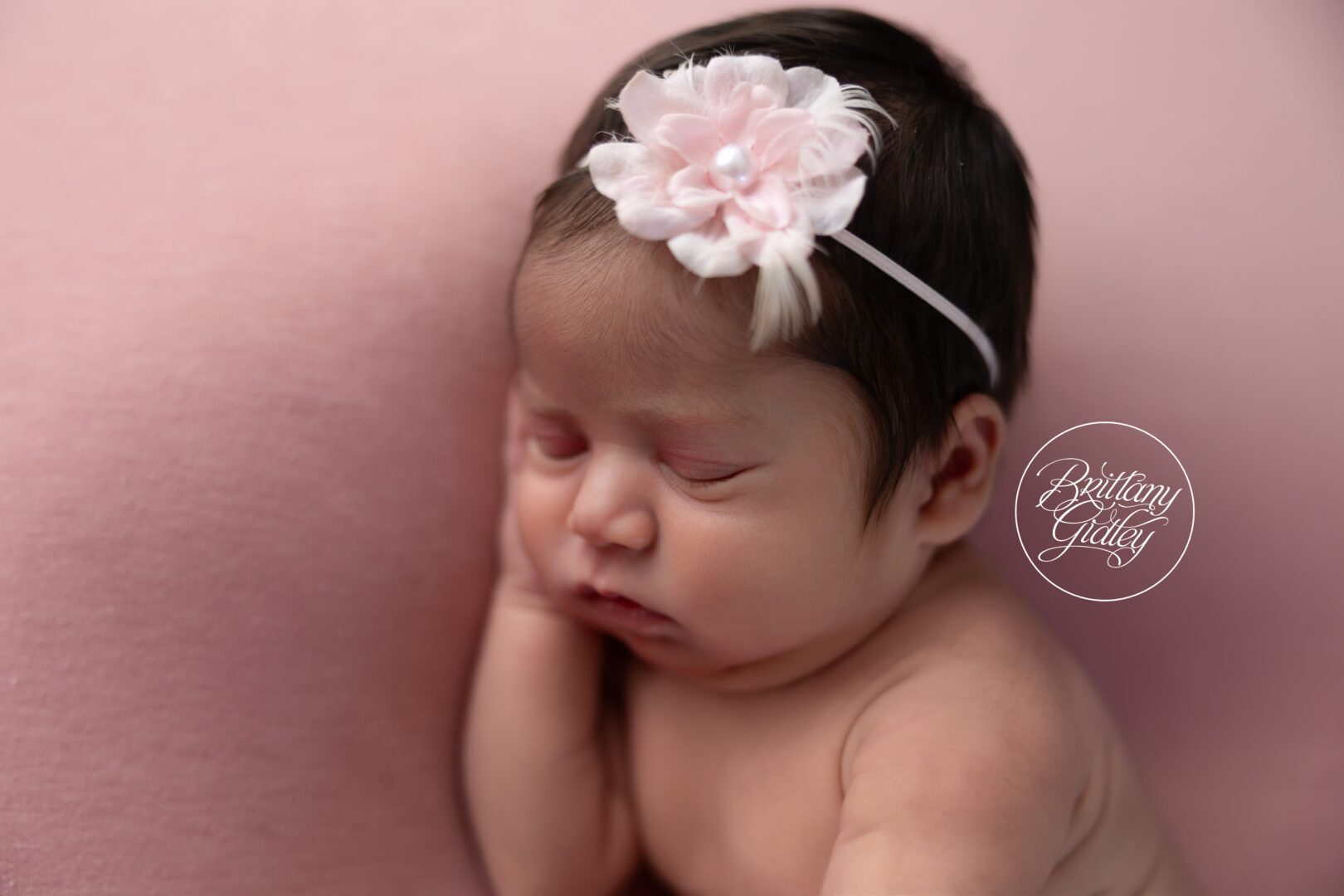 Close-up of newborn Ava sleeping with her hand under her cheek on pink